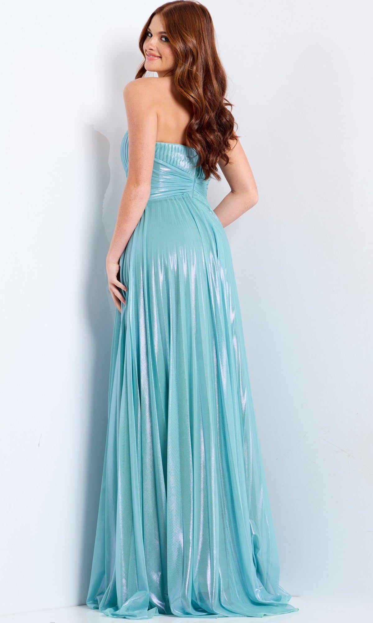 A woman with long red hair models the Jovani 39023 long prom dress—a strapless, floor-length gown in light blue shimmer with a pleated bodice—as she stands and looks over her shoulder.